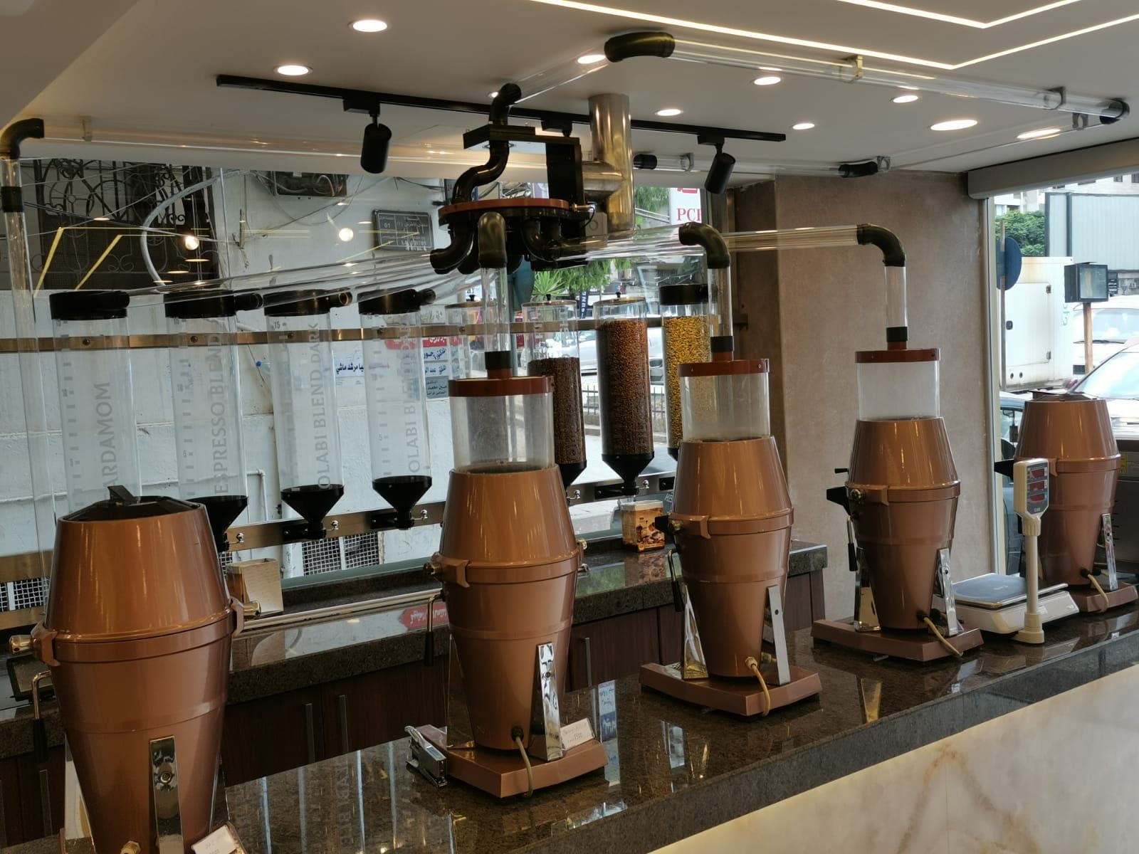 Coffee shop counter with clear plexi bean pipelines running overhead into a row of copper grinders